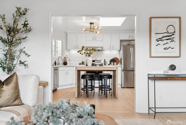 kitchen with a chandelier, decorative backsplash, appliances with stainless steel finishes, white cabinets, and a sink