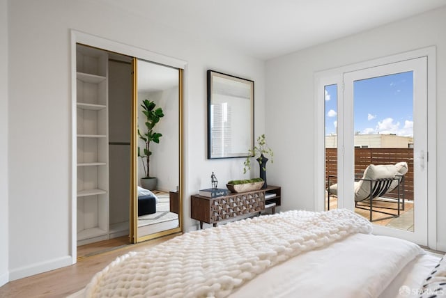 bedroom with a closet, wood finished floors, baseboards, and access to exterior