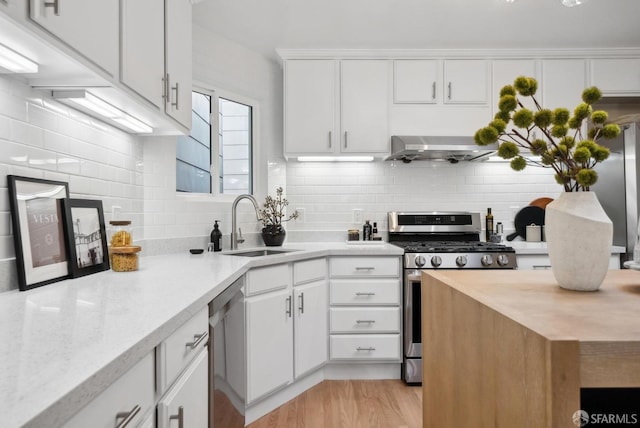 kitchen featuring tasteful backsplash, extractor fan, light wood-style flooring, appliances with stainless steel finishes, and a sink