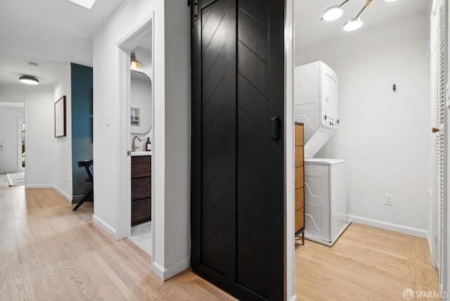 hall with light wood-style flooring, stacked washer / drying machine, and baseboards