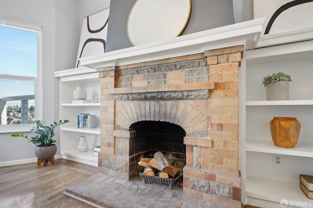 detailed view of a fireplace, wood finished floors, built in features, and baseboards