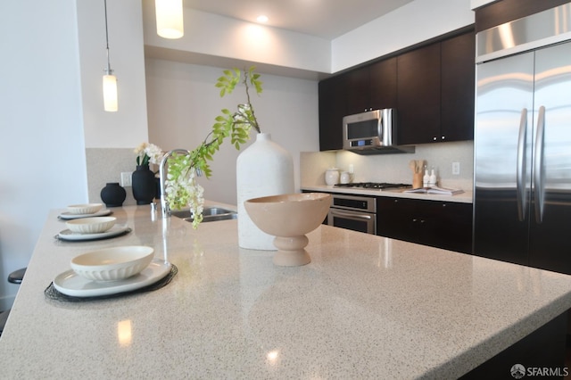 kitchen featuring light stone counters, tasteful backsplash, appliances with stainless steel finishes, a sink, and a peninsula