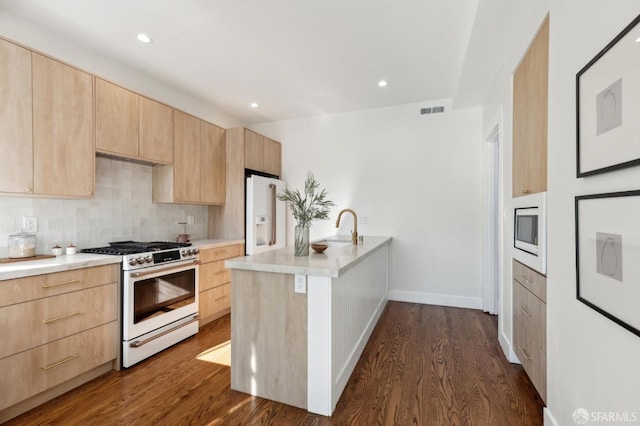 kitchen featuring backsplash, kitchen peninsula, white appliances, light brown cabinets, and dark hardwood / wood-style flooring