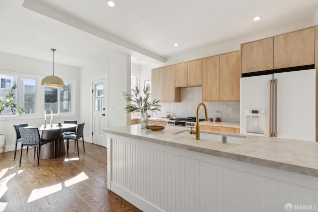 kitchen featuring white fridge with ice dispenser, light brown cabinets, sink, hanging light fixtures, and light stone counters