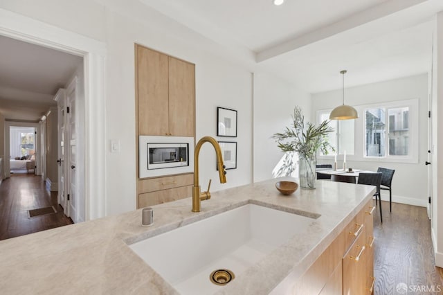 kitchen with dark hardwood / wood-style floors, light brown cabinets, hanging light fixtures, light stone countertops, and sink