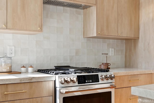 kitchen with wall chimney exhaust hood, light brown cabinetry, backsplash, and stainless steel gas range oven