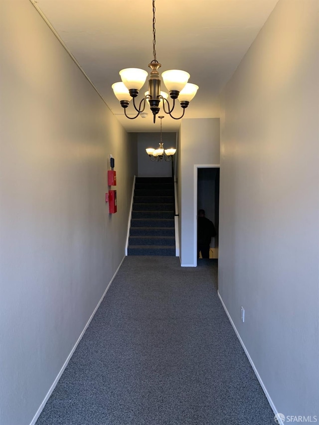 hall with baseboards, stairway, dark carpet, and a notable chandelier