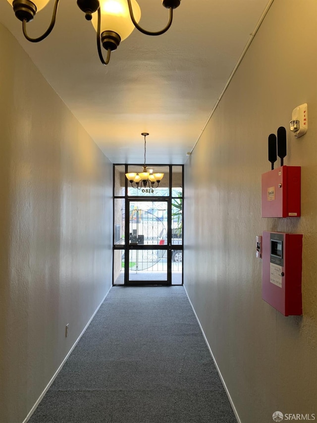 hallway featuring baseboards, floor to ceiling windows, carpet, and an inviting chandelier