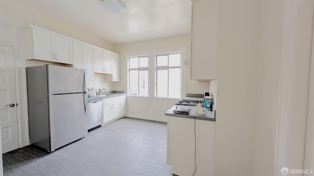 kitchen featuring appliances with stainless steel finishes, light wood-type flooring, white cabinets, and a sink