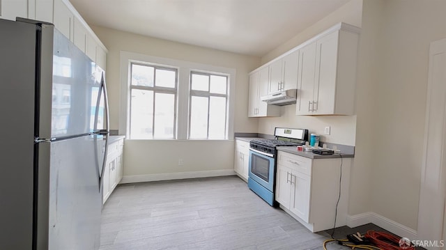 kitchen with light wood finished floors, baseboards, appliances with stainless steel finishes, under cabinet range hood, and white cabinetry