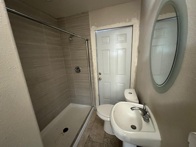 bathroom featuring sink, a tile shower, and toilet