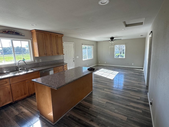 kitchen featuring sink, dark hardwood / wood-style floors, a kitchen island, stainless steel dishwasher, and dark stone counters