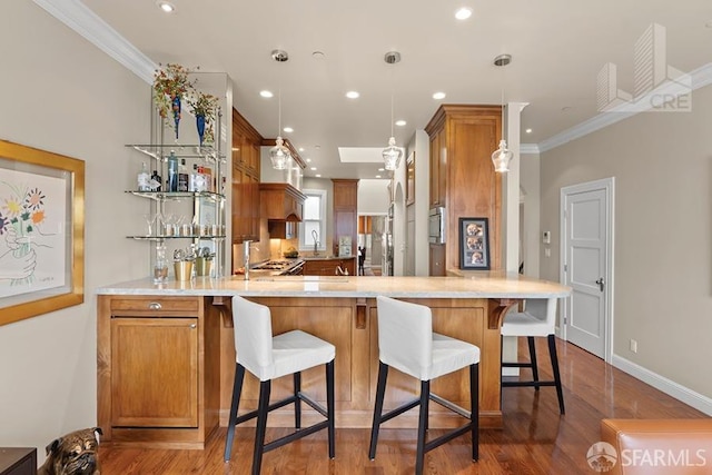 kitchen featuring pendant lighting, kitchen peninsula, sink, hardwood / wood-style flooring, and ornamental molding