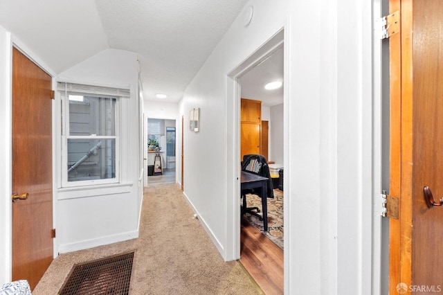 hallway featuring a textured ceiling, light carpet, and lofted ceiling