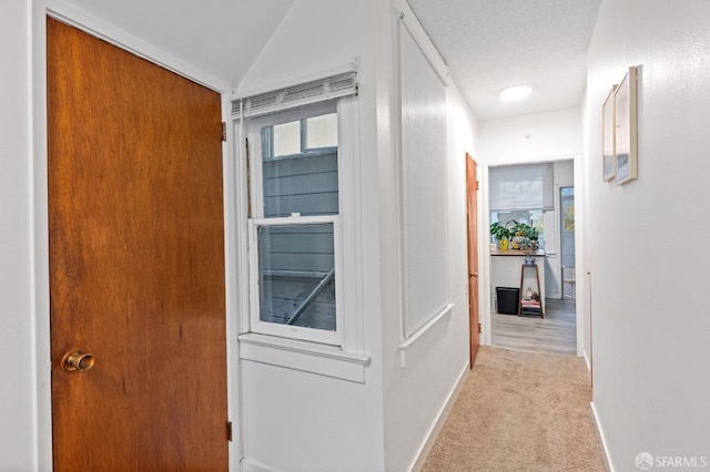 corridor featuring a textured ceiling, light carpet, a wealth of natural light, and vaulted ceiling