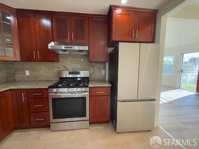 kitchen with stainless steel gas stove, decorative backsplash, and refrigerator