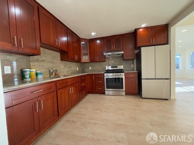 kitchen with sink, white refrigerator, backsplash, and stainless steel range with gas cooktop