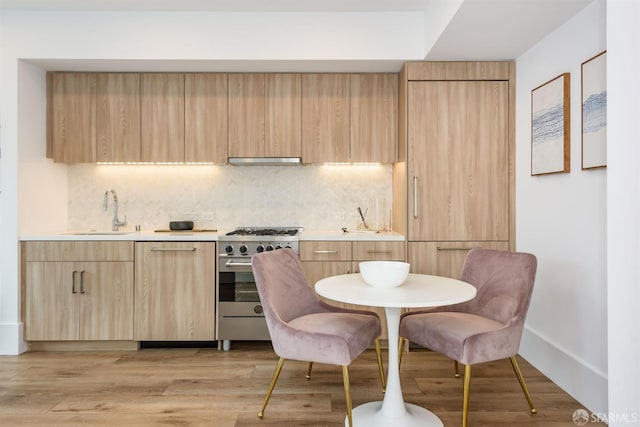 kitchen with light wood-type flooring, under cabinet range hood, light brown cabinets, and stainless steel stove