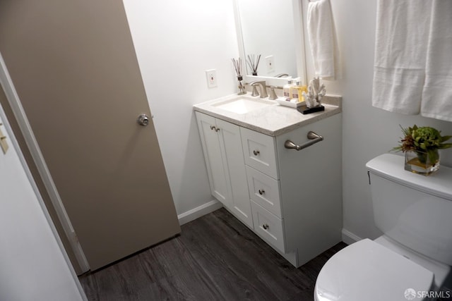 half bath featuring vanity, toilet, wood finished floors, and baseboards