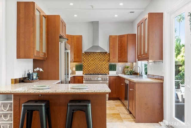 kitchen featuring wall chimney range hood, brown cabinets, a peninsula, and a sink