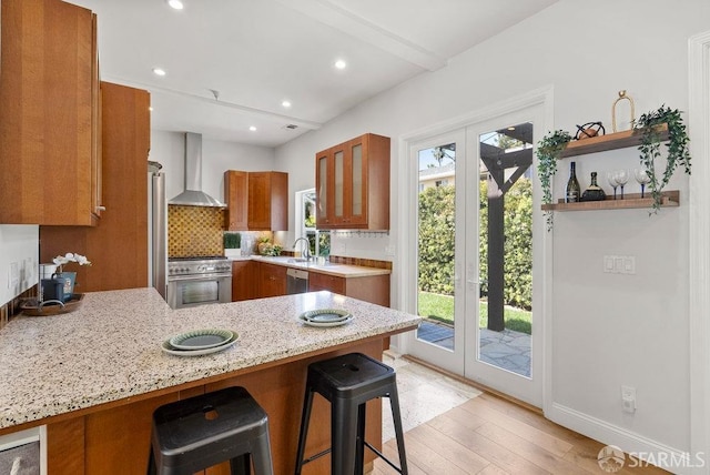 kitchen featuring appliances with stainless steel finishes, brown cabinets, a peninsula, a breakfast bar, and wall chimney exhaust hood