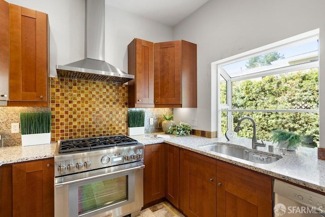 kitchen with brown cabinetry, light stone countertops, wall chimney exhaust hood, a sink, and stainless steel appliances