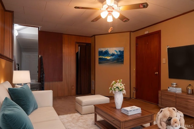 living room with ornamental molding, wooden walls, light carpet, and ceiling fan