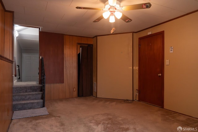 carpeted spare room featuring crown molding, ceiling fan, and wooden walls