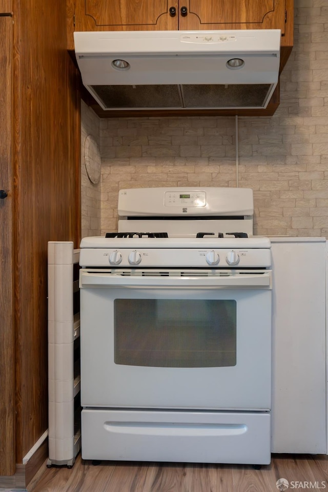 kitchen with white range with gas cooktop, hardwood / wood-style flooring, and brick wall