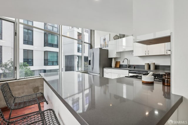 kitchen with white cabinets, sink, stainless steel fridge, gas stovetop, and a kitchen bar