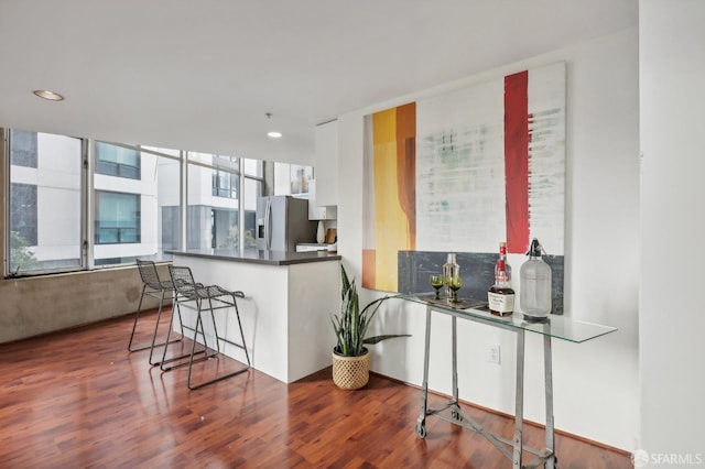 kitchen featuring white cabinets, a kitchen breakfast bar, stainless steel fridge, dark hardwood / wood-style flooring, and kitchen peninsula