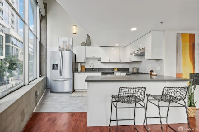 kitchen featuring a kitchen bar, kitchen peninsula, stainless steel appliances, sink, and white cabinets