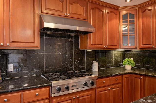 kitchen featuring dark stone counters, stainless steel gas stovetop, glass insert cabinets, and under cabinet range hood