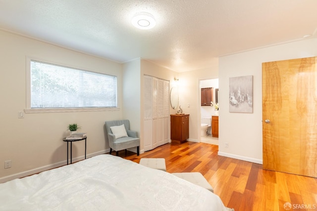 bedroom featuring baseboards, connected bathroom, light wood-style flooring, and a textured ceiling