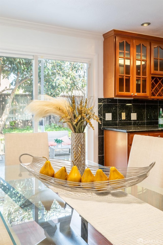 kitchen with tasteful backsplash, brown cabinetry, glass insert cabinets, and crown molding