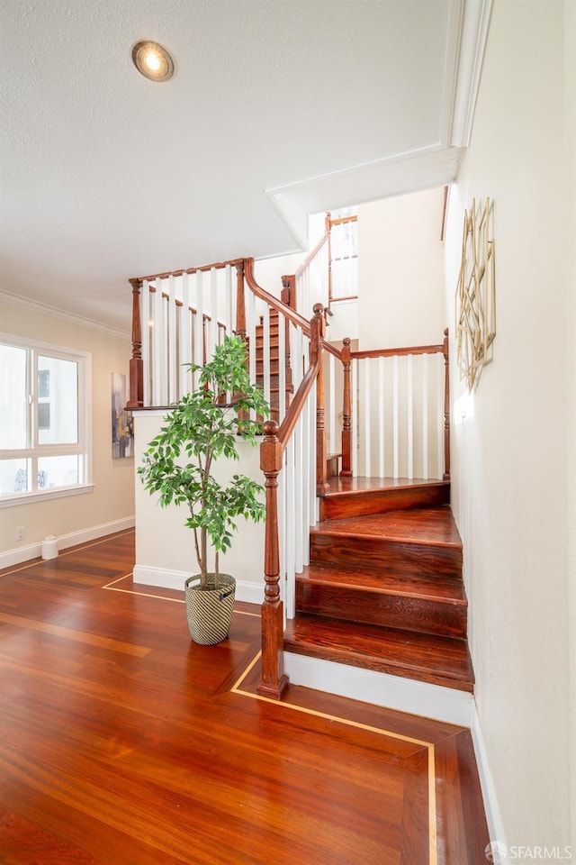 staircase featuring crown molding, a textured ceiling, baseboards, and wood finished floors