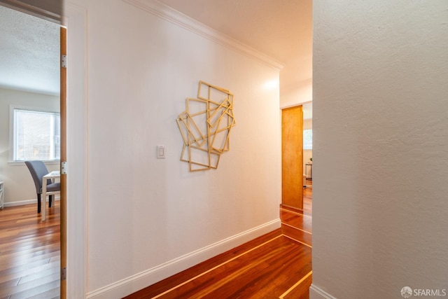 hall with dark wood-style floors, a textured wall, crown molding, and baseboards