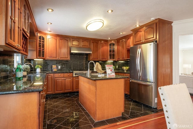 kitchen featuring recessed lighting, under cabinet range hood, granite finish floor, freestanding refrigerator, and tasteful backsplash