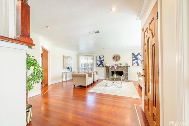 living room with a fireplace, wood finished floors, visible vents, baseboards, and crown molding