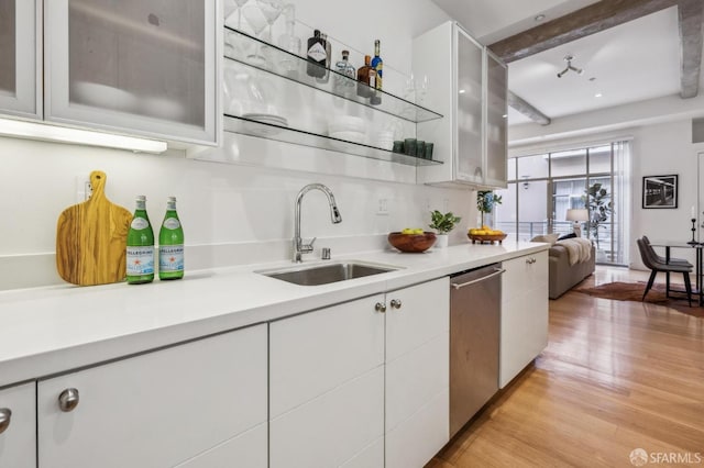 kitchen with beamed ceiling, sink, white cabinets, stainless steel dishwasher, and light wood-type flooring