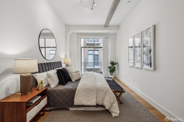 bedroom featuring beamed ceiling, rail lighting, hardwood / wood-style floors, and access to exterior