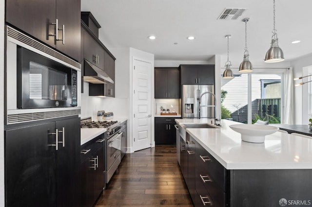 kitchen featuring hanging light fixtures, sink, an island with sink, stainless steel appliances, and dark hardwood / wood-style floors