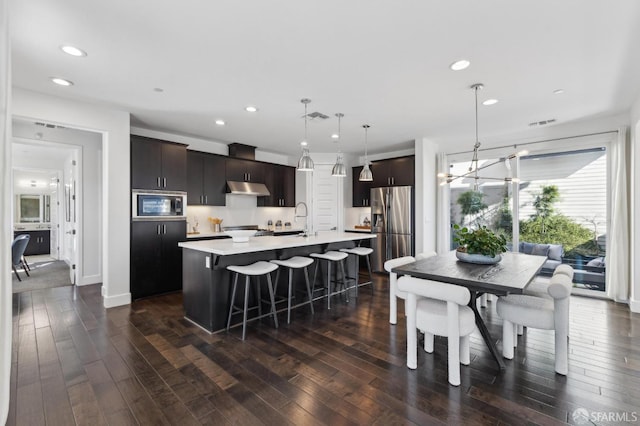 kitchen featuring stainless steel fridge with ice dispenser, black microwave, decorative light fixtures, a center island with sink, and dark hardwood / wood-style floors