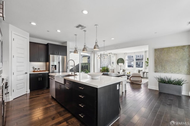 kitchen featuring hanging light fixtures, sink, dark wood-type flooring, stainless steel appliances, and a center island with sink