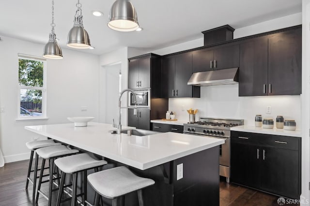 kitchen featuring stainless steel range, dark hardwood / wood-style flooring, an island with sink, sink, and hanging light fixtures