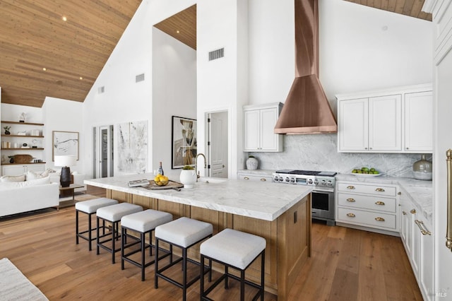 kitchen with wooden ceiling, white cabinets, high end stove, and an island with sink