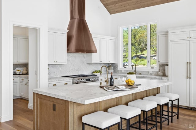 kitchen featuring wooden ceiling, a kitchen island with sink, lofted ceiling, wall chimney exhaust hood, and white cabinets