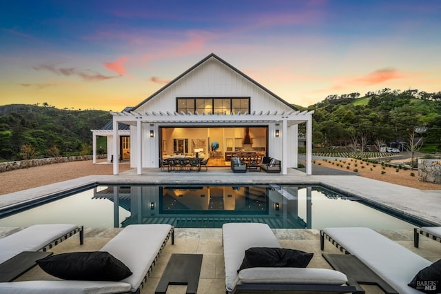 back house at dusk featuring a pergola, an outdoor structure, and a patio