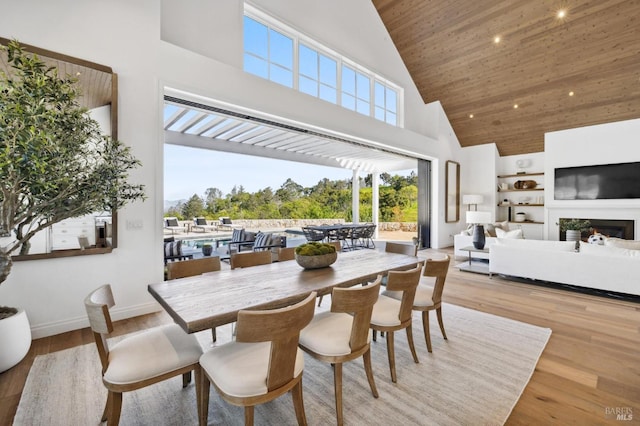 dining space with built in shelves, wood ceiling, a towering ceiling, and light hardwood / wood-style flooring