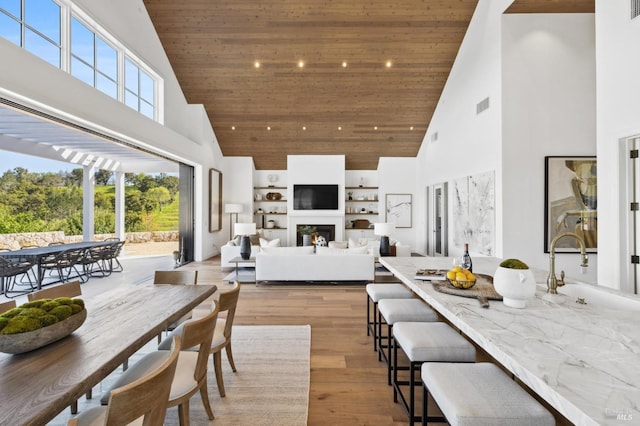 dining area featuring high vaulted ceiling, light hardwood / wood-style floors, sink, and wood ceiling